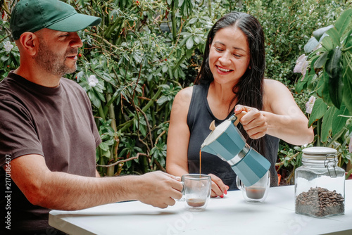 Konstfotografi Couple sharing a relaxed coffee moment outdoors as a man pours freshly brewed coffee for a smiling woman surrounded by lush vegetation