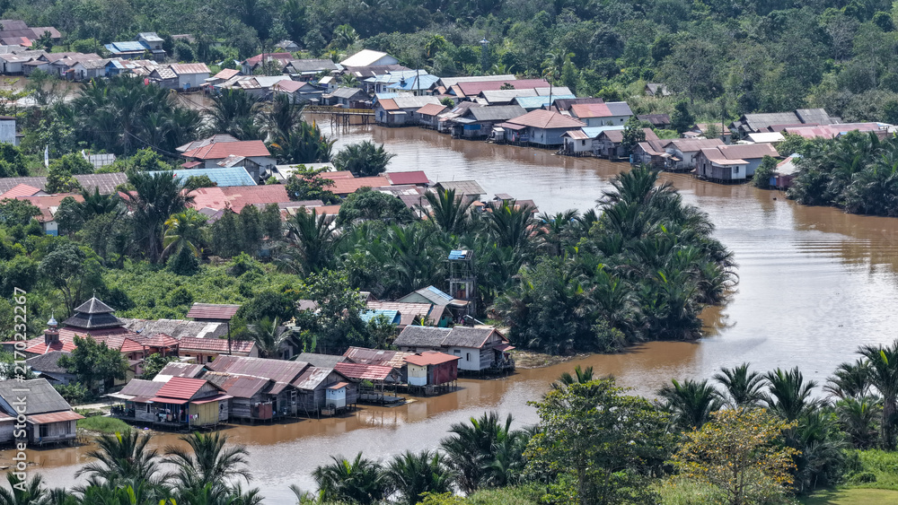 Fototapeta premium Traditional stilt houses along a riverbank in a tropical village landscape in South Kalimantan