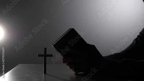 Obraz na płótnie Person silhouette holding a bible in prayer, bathed in a single shaft of lightco