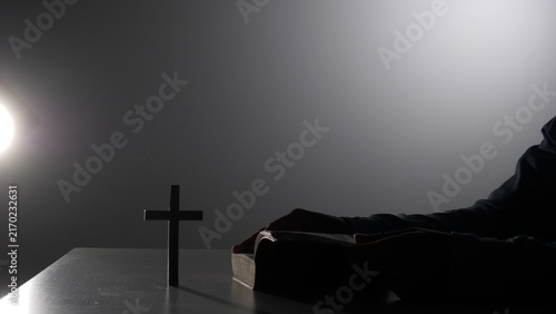 Photography Silhouette of a person with hands on a bible, offering a silent prayer next to a