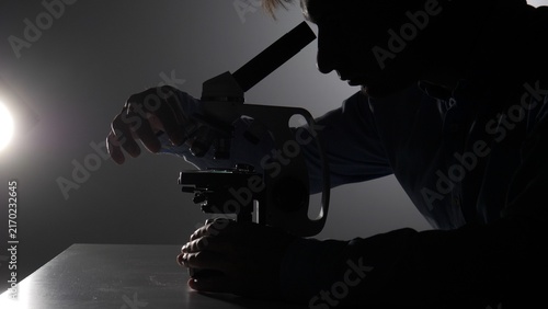 Bild auf Leinwand Scientist in silhouette meticulously using a professional microscope on a labora