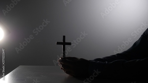 Quadro su tela Person's hands holding a wooden cross against a dark background, reflecting conc