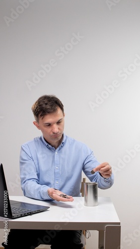 Foto Man in a blue shirt sitting at a white desk, carefully putting coins from his ha