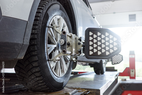 Obraz na plátne Winter tire replacement for SUV with studded wheel in service bay, alignment sensor fixed on front axle for seasonal maintenance, traction control and cold weather safety