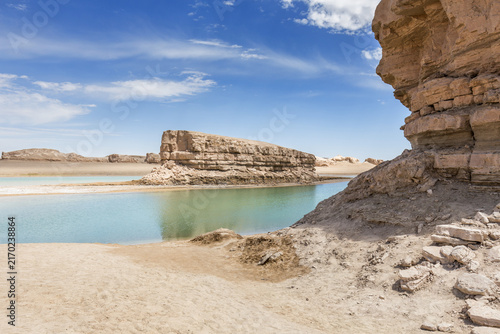 Obraz na płótnie Layered rock formations and water-filled yardang in arid desert under clear blue sky