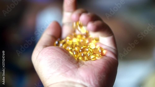 Close-up of a human hand holding a pile of golden yellow softgel fish oil capsules.	