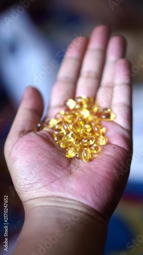 Close-up of a human hand holding a pile of golden yellow softgel fish oil capsules.	