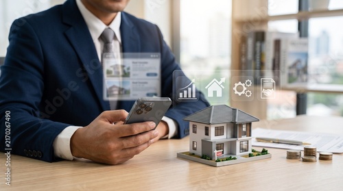 Businessman using smartphone app for real estate searching, virtual holographic screen overlay, model house on office desk