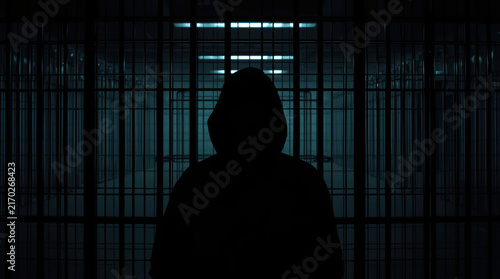 Anonymous individual silhouette behind metal bars creates mysterious prison scene