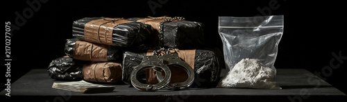 Illegal Substances and Handcuffs: A pile of tightly wrapped bricks, likely containing illicit drugs, sits next to a bag of white powder and a pair of handcuffs.