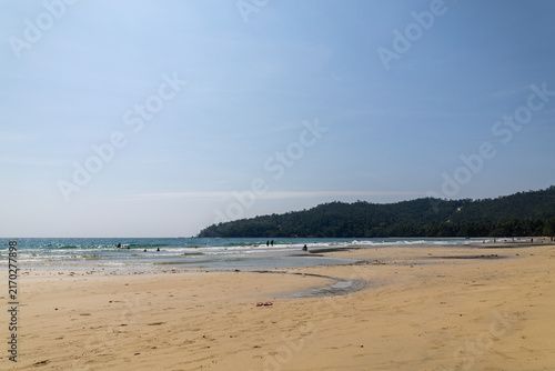 Wide sandy beach with ocean waves, swimmers and forested headland