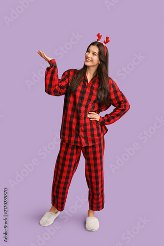 Beautiful young woman in checkered pajamas and reindeer horns on purple backg...