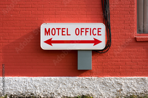 A white sign with red text reading MOTEL OFFICE and a double-sided arrow mounted on a vibrant red brick wall. Perfect for travel or hospitality concepts.