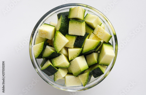 Konstfotografi Top view of fresh diced green zucchini pieces served in a clear glass bowl on a white background