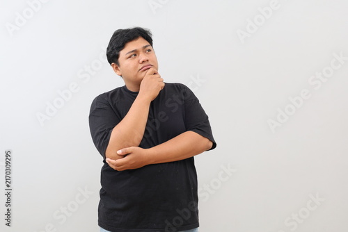 Foto A heavy-set man stands against a white background, holding his chin and gazing into the empty space beside him while deep in thought