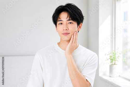 頬に手を添えて肌の状態を確かめる20代の日本人男性