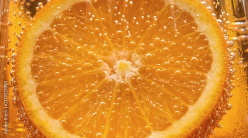 Close-up of a vibrant orange slice submerged in sparkling water with many tiny bubbles.