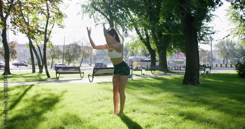 Stretching workout. Outdoor training. Slim female practicing healthy physical activity doing exercise in natural light green park.