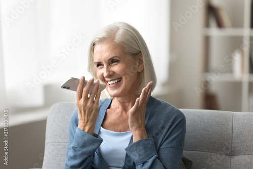 Voice app. Cheerful excited elderly woman grandmother hold smartphone by mouth dictate request to virtual assistant record vocal message. Happy aged lady use phone loudspeaker for easy communication