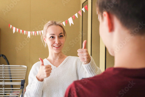 Cuadro en lienzo Happy Woman In White Sweater Smiles At Her Reflection While Giving Double Thumbs
