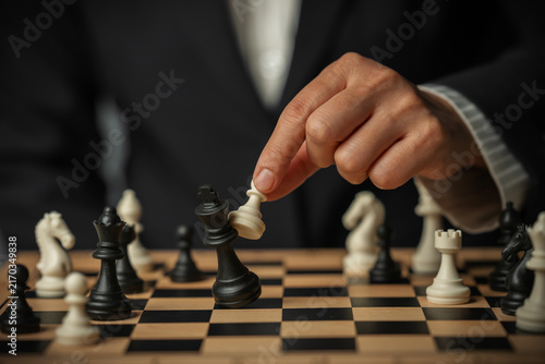 Obraz na płótnie business hand holding white chess pawn taking black king, checkmate concept