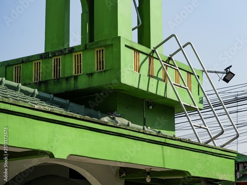 Green painted mosque building rooftop architecture with access ladder and outdoor spotlight against blue sky.