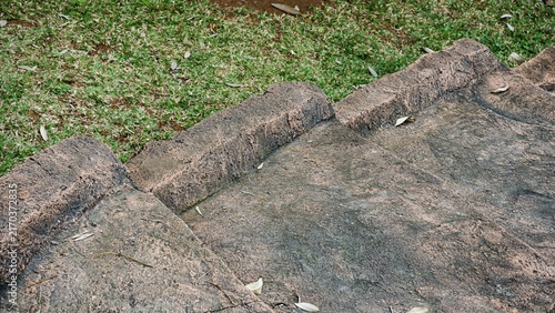 Rough concrete garden steps surrounded by green grass lawn and fallen dry leaves in daylight.