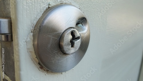 Close-up of a damaged house door lock showing clear signs of forced entry attempt, scratched metal surface, broken keyhole.