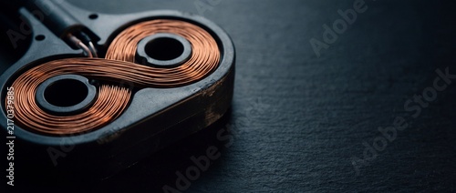 Close-up of a dark object with exposed copper wire coils, used in electrical circuits or scientific experiments.