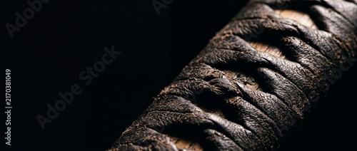 Close up view of ancient samurai katana sword hilt featuring intricate dark leather wrapped handle and traditional craftsmanship.