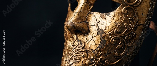 Cracked gold venetian mask with intricate baroque floral patterns on dark background represents classic carnival masquerade style.