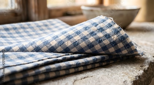 Folded blue and white checkered linen fabric rests on stone surface.