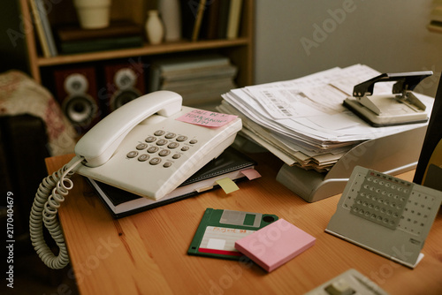 Retro office desk featuring vintage landline telephone, floppy disk, and paper documents. Concept of nostalgic corporate communication and old school business workflow, close up shot