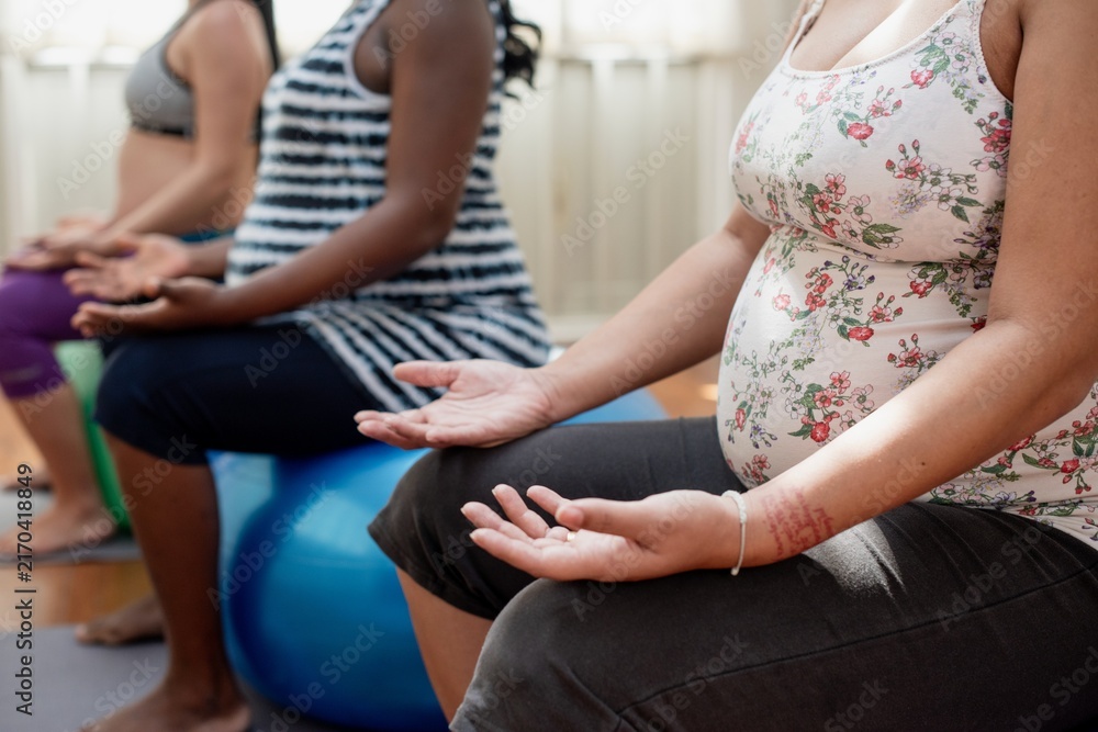 Fototapeta premium Pregnant women of diverse ethnicities practicing prenatal yoga indoors.