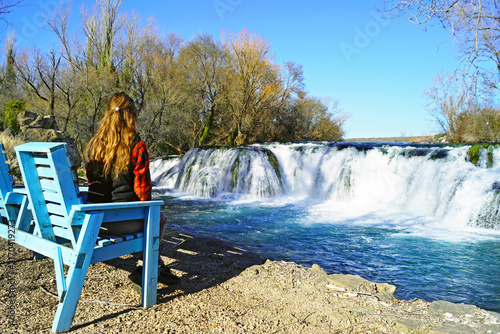Fotografía Long-haired woman sitting on wooden armchair admiring view of Kočuša Waterfall