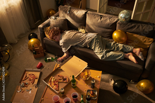 Konstfotografi Caucasian young adult man sleeping on sofa in messy room after party, high angle view