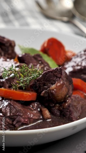 beef bourguignon stew with carrots and thyme in red wine sauce on white plate, vertical video