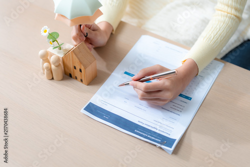 Fotografie Home insurance concept with a person completing an application beside a wooden house and family under an umbrella, protection, coverage, security, policy, safety