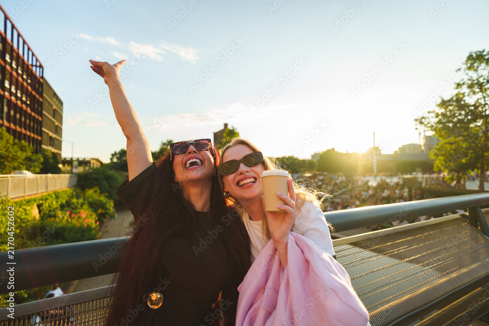 Obraz premium Two friends laughing, having fun outdoors with takeaway coffee at golden hour