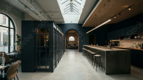 Modern office interior featuring phone booth pods and a long communal counter with bar stools in a flexible workspace