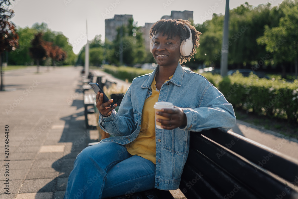 Obraz premium Young woman enjoying music and coffee in park