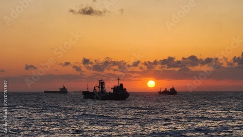 Fotografie East Sea Sunrise with Ships: An East Sea sunrise featuring silhouettes of ships sailing across the horizon beneath a glowing morning sun, adding a lively touch to the ocean view