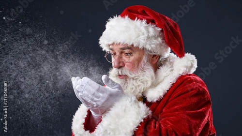Elderly man in Santa costume blowing snow from gloved hands in studio portrait
