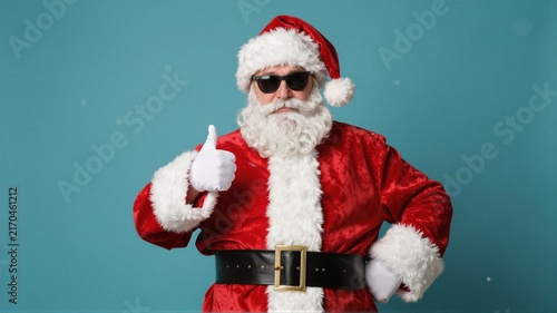 Santa figure wearing red suit and sunglasses giving thumbs up on teal background