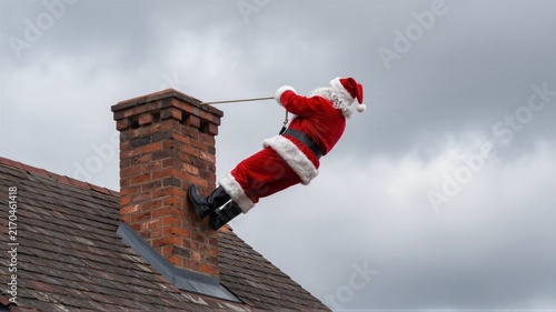 Santa costume figure climbing brick chimney on rooftop against cloudy sky