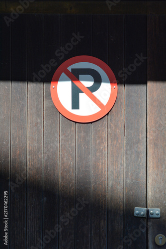 Foto A round red and white no parking sign with the letter P is attached to a vertical dark wooden plank gate partly illuminated by a sharp beam of sunlight