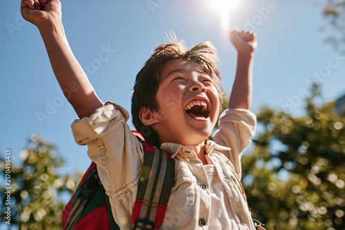 Extremely joyful schoolboy laughing with arms raised in celebration outdoors