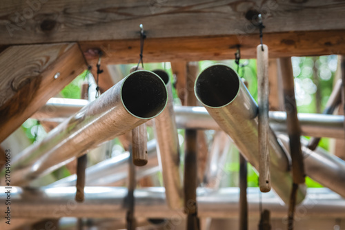 Metal tubes hang from wooden structures in a garden in the afternoon light