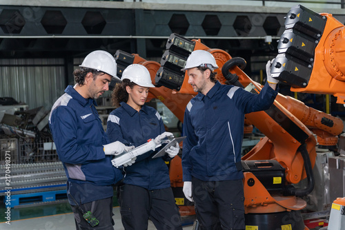 Engineers wearing hardhats using laptop computer to inspect and program robotic arm system in factory.