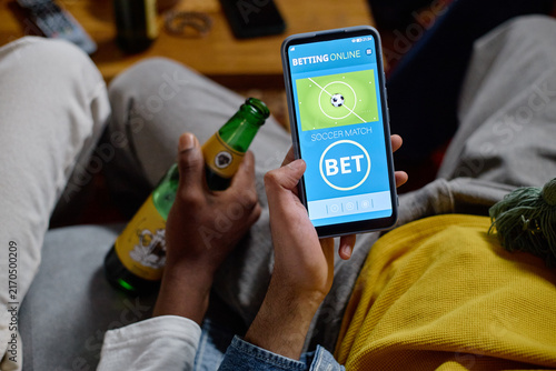 Obraz na płótnie Diverse young adult male football fans holding beer bottle and using online betting app on smartphone